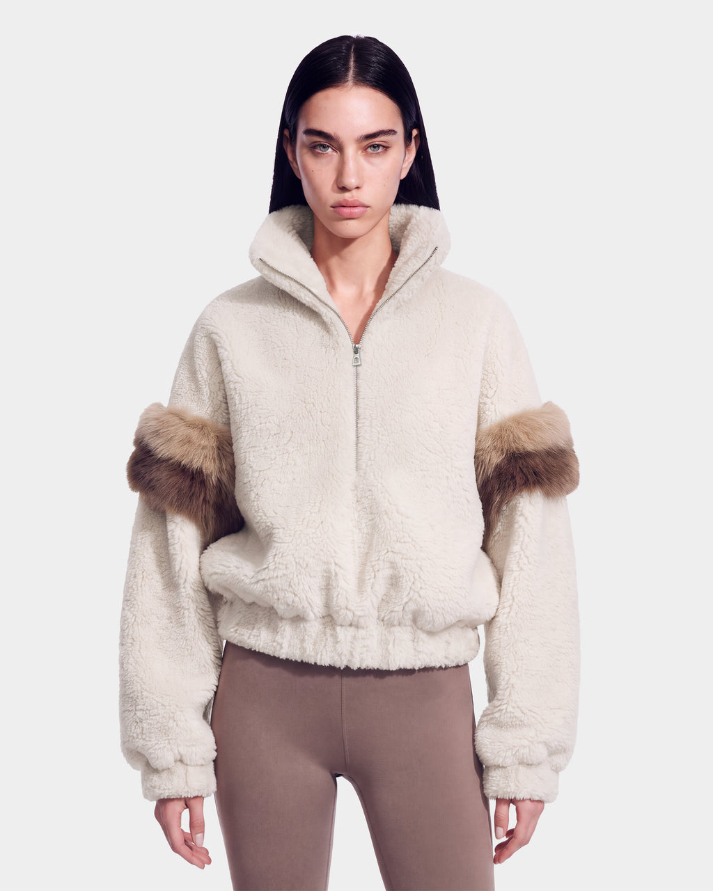A woman models the Rudsak ALEIA - 8526693 Vanilla, a cream-colored fleece zip-up jacket with fur trim on the upper sleeves, paired with taupe leggings. She stands against a plain light background, looking directly at the camera.