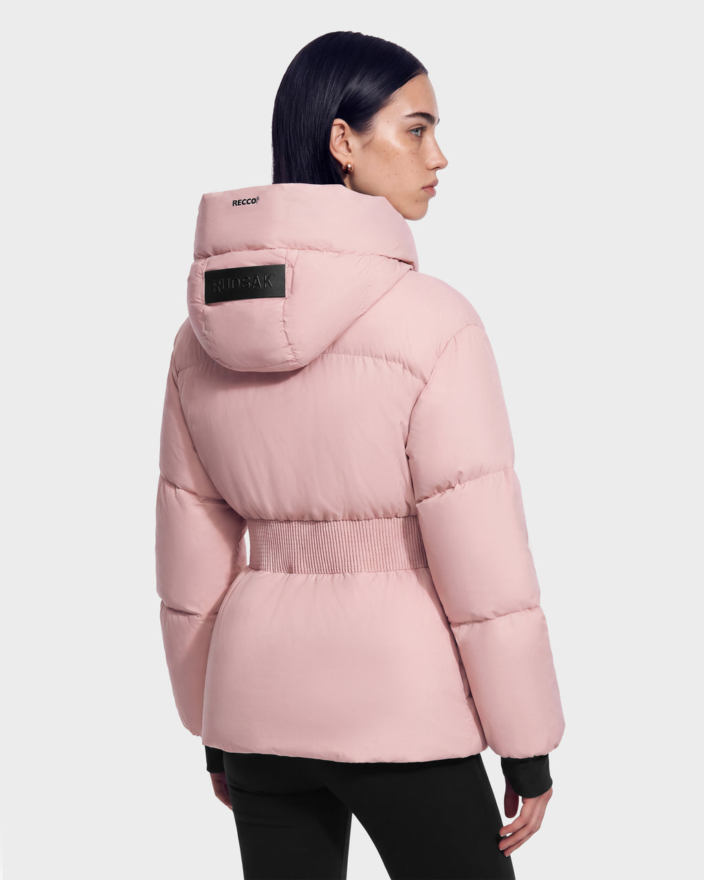 Person wearing a pink Rudsak DIAMOND - 8126772 Vintage Rose quilted puffer coat with a cinched elastic waist and a black logo patch on the hood.