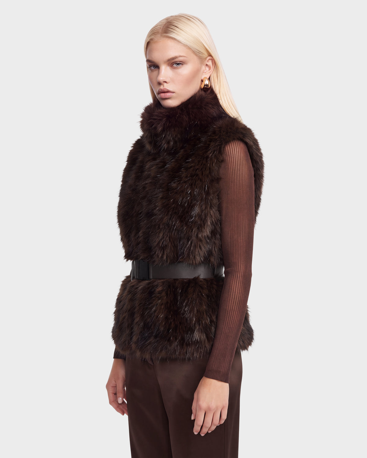 A person wearing a Rudsak MAULIN - 8524611 Mix Espresso dark brown faux fur vest cinched with a wide vegan leather belt over a matching mock-neck pullover.