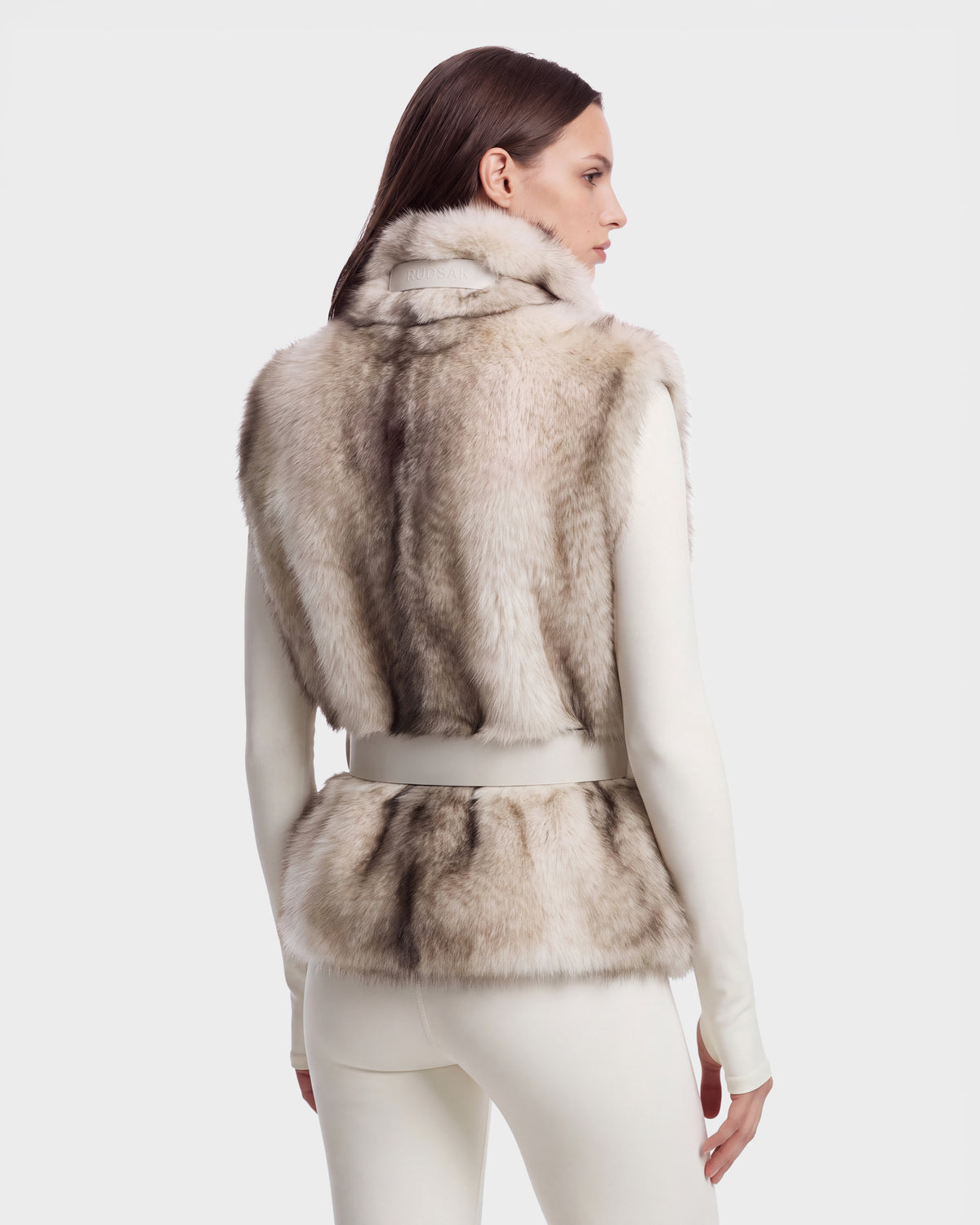 A woman seen from the back wearing a chic MAULIN - 8524611 Mix Vanilla faux fur vest with a belted waist over a long-sleeved white top.