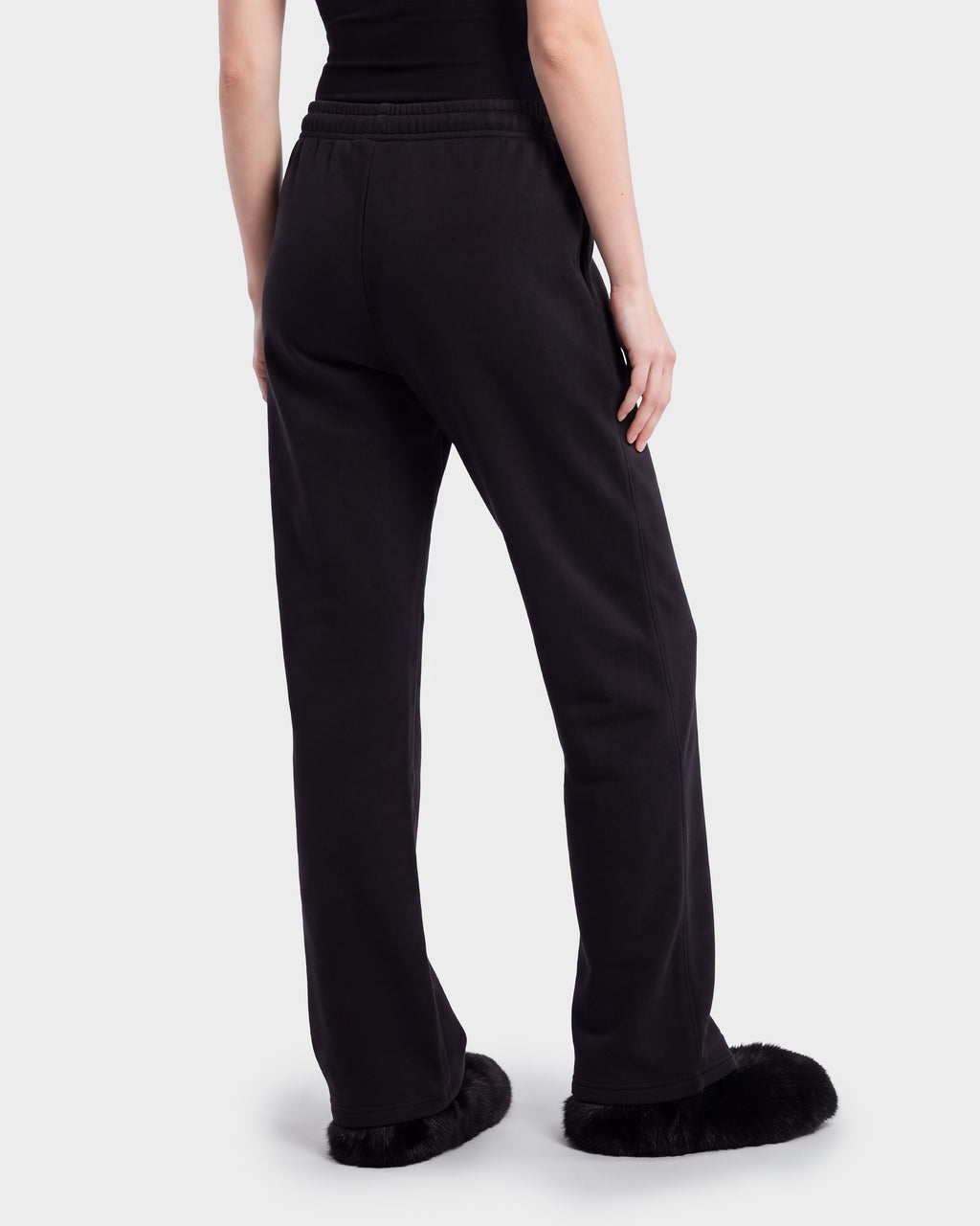 A person seen from behind wearing RUDSAK ANGEL - 8526725 Black sweatpants with a drawstring waist and black fur-trimmed slip-on shoes.
