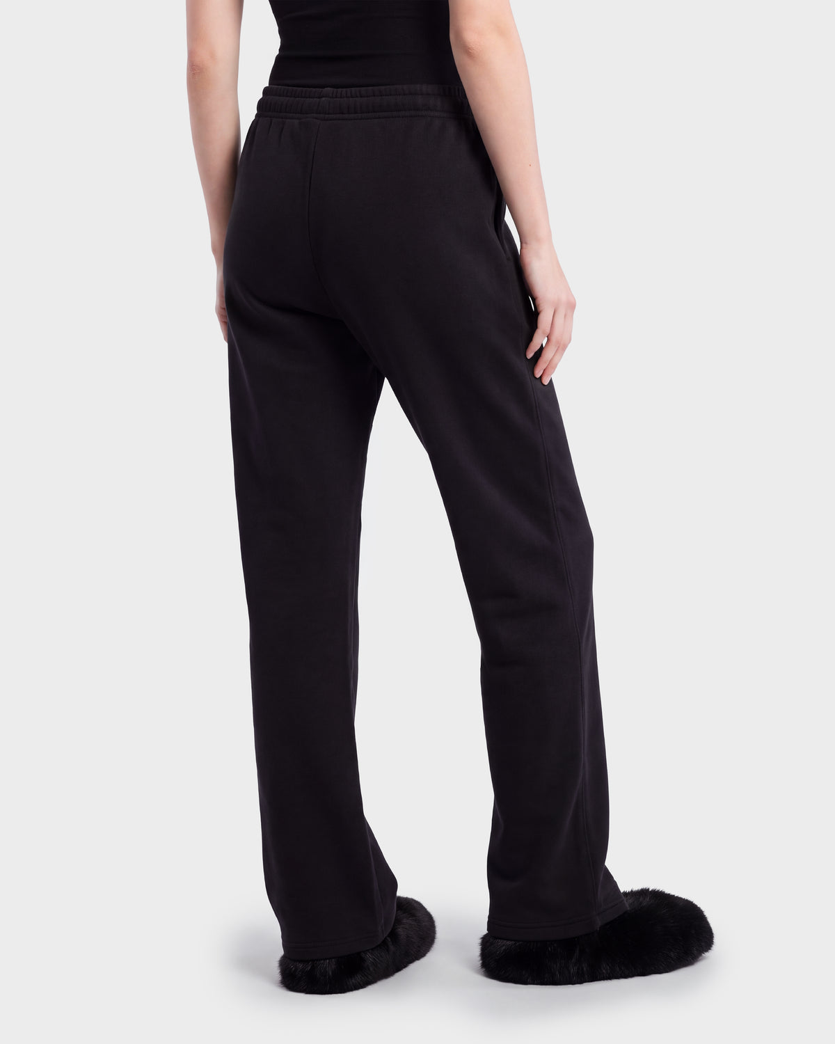 A person seen from behind wearing RUDSAK ANGEL - 8526725 Black sweatpants with a drawstring waist and black fur-trimmed slip-on shoes.