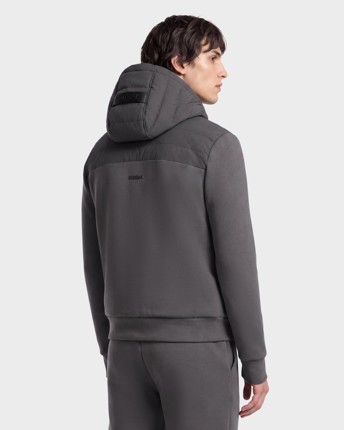 A man seen from behind wearing a grey DEE MAT - 6124028 Rudsak urban jacket with a quilted top section and a logo on the hood and back.
