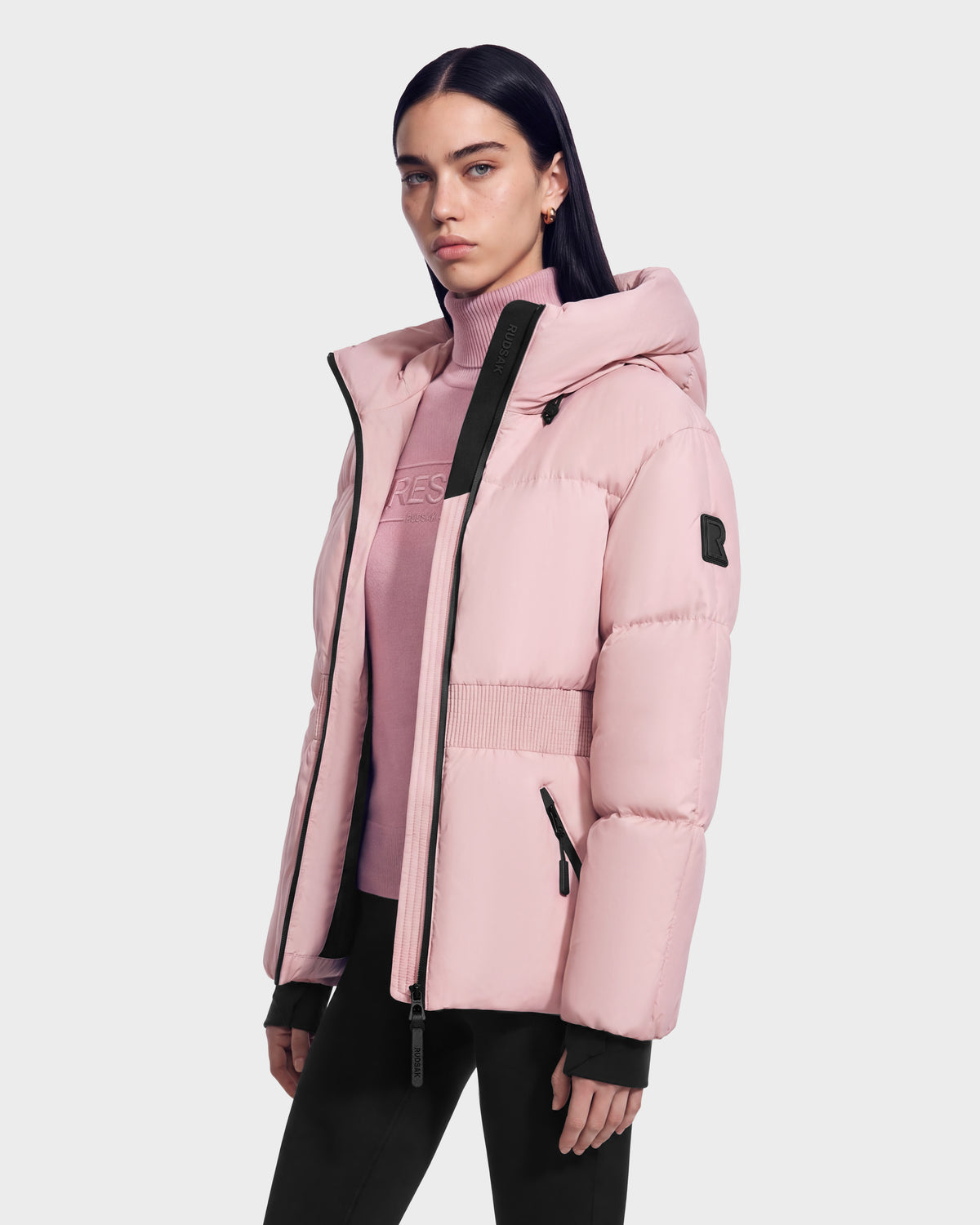 Model wearing a Rudsak DIAMOND - 8126772 Vintage Rose light pink quilted puffer hooded jacket with black zipper detailing over a matching pink mock-neck sweater.