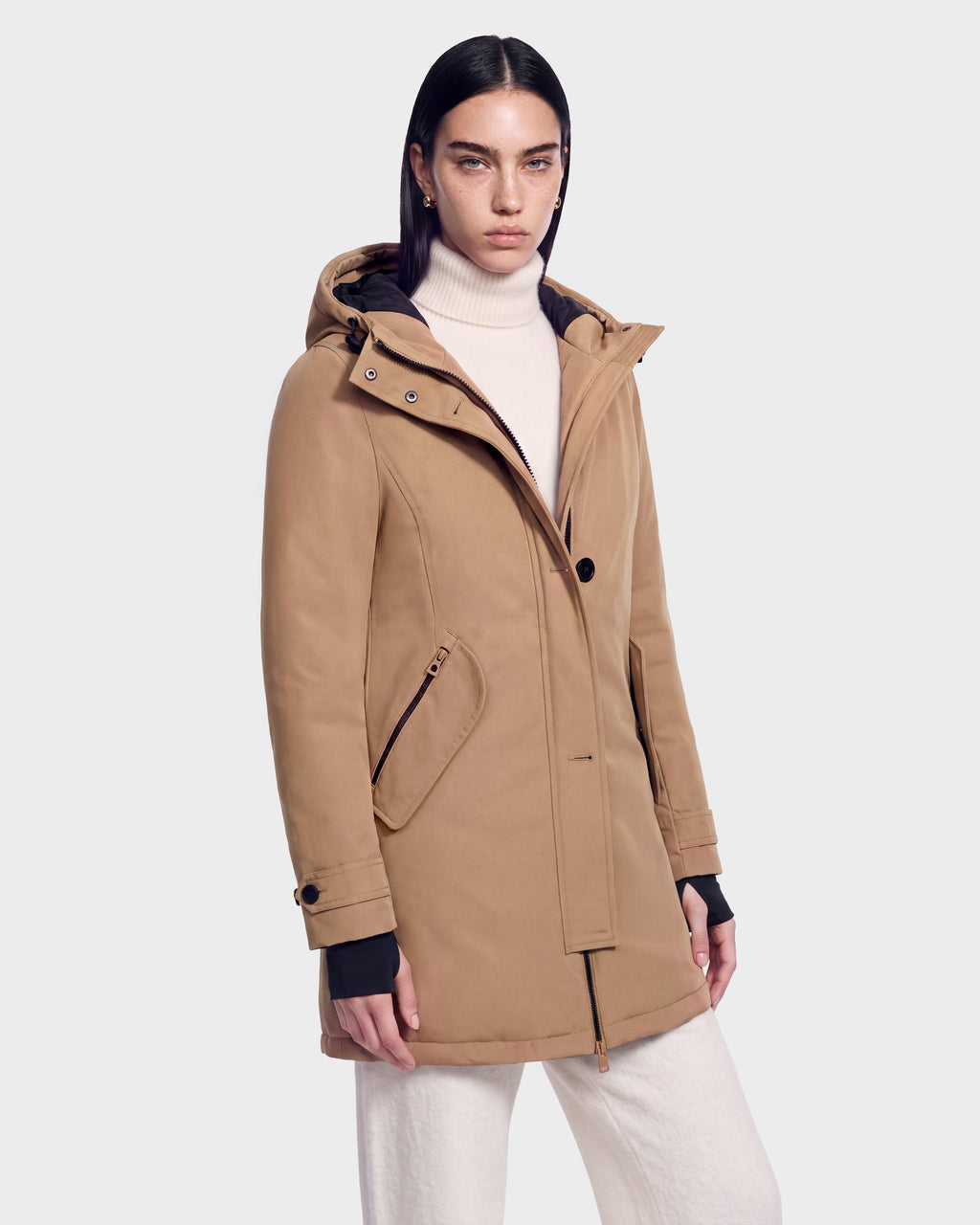 A person wears the Rudsak KEYSHIA - 8126517 Camel coat over a white turtleneck and pants, standing against a plain light background and looking at the camera with a neutral expression.