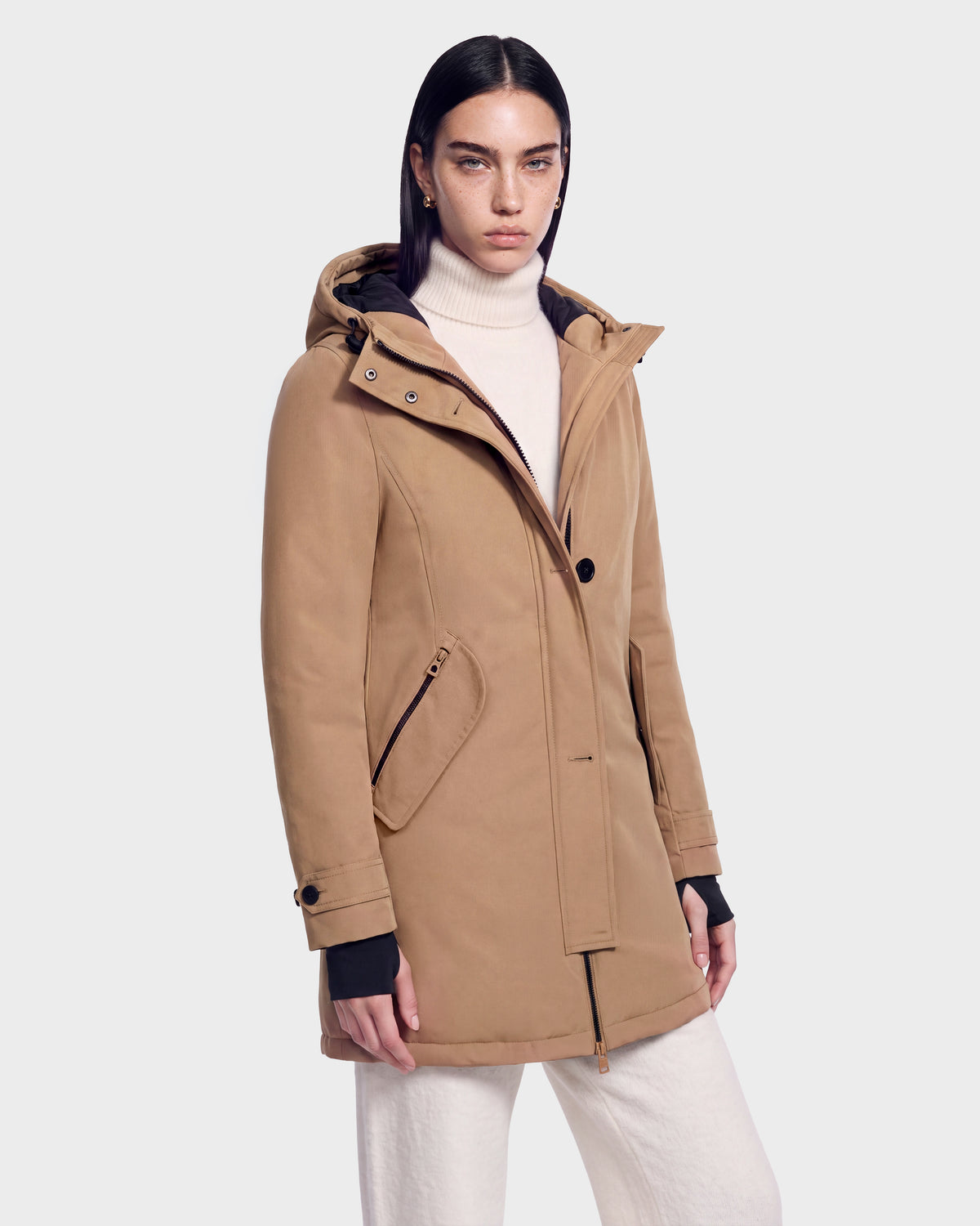 A person wears the Rudsak KEYSHIA - 8126517 Camel coat over a white turtleneck and pants, standing against a plain light background and looking at the camera with a neutral expression.