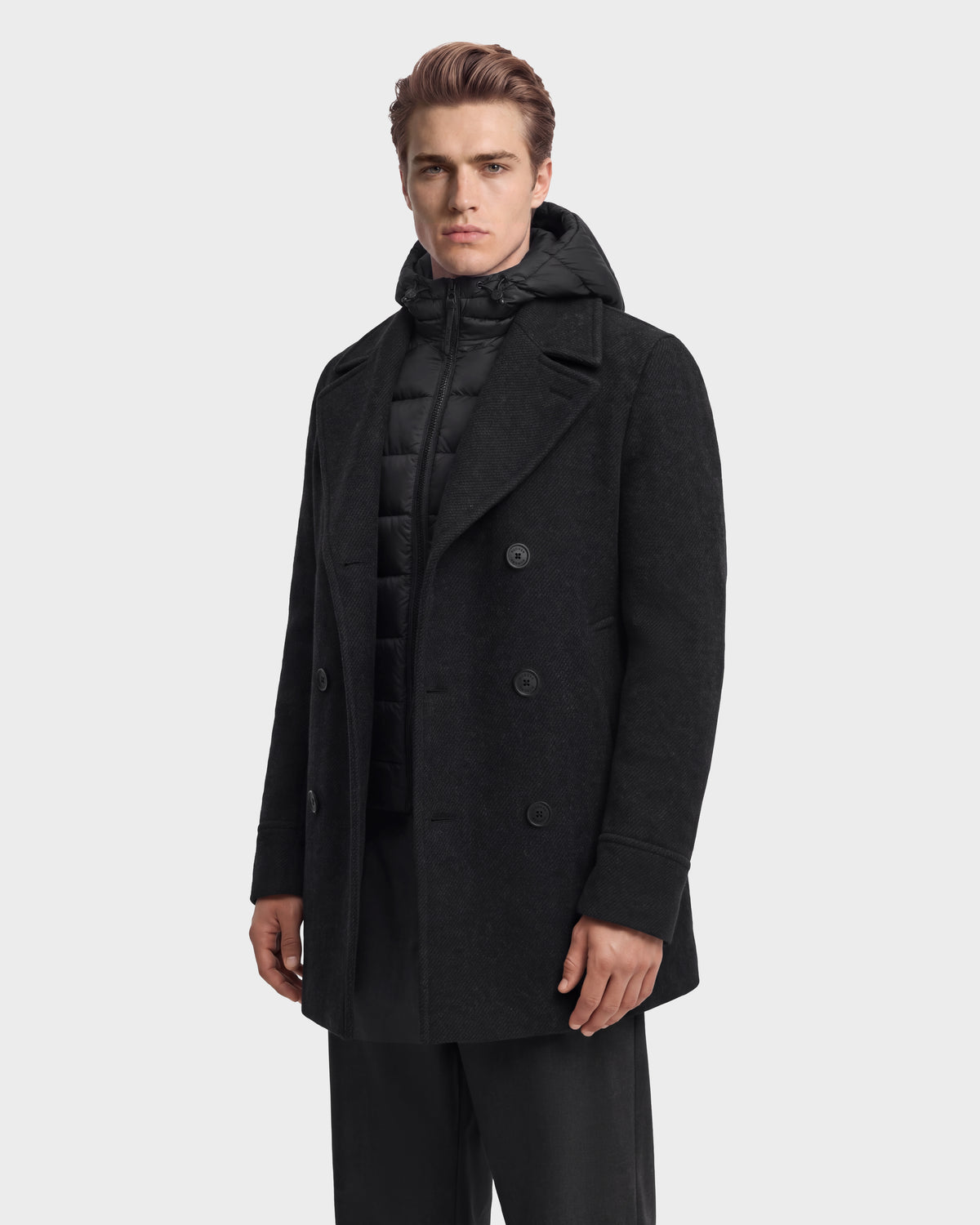 A man wearing a charcoal LUCIEN - 6126508 wool-blend pea coat over a black quilted hooded vest with duck down insulation.