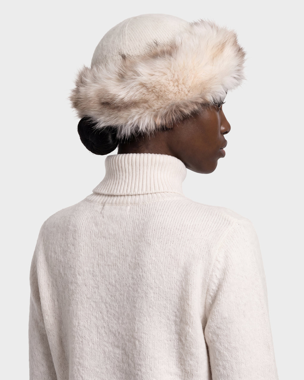 A cream-colored LORETTA W - 8426510 Vanilla RUDSAK pillbox hat with a plush faux fur trim worn by a person in a matching turtleneck sweater.
