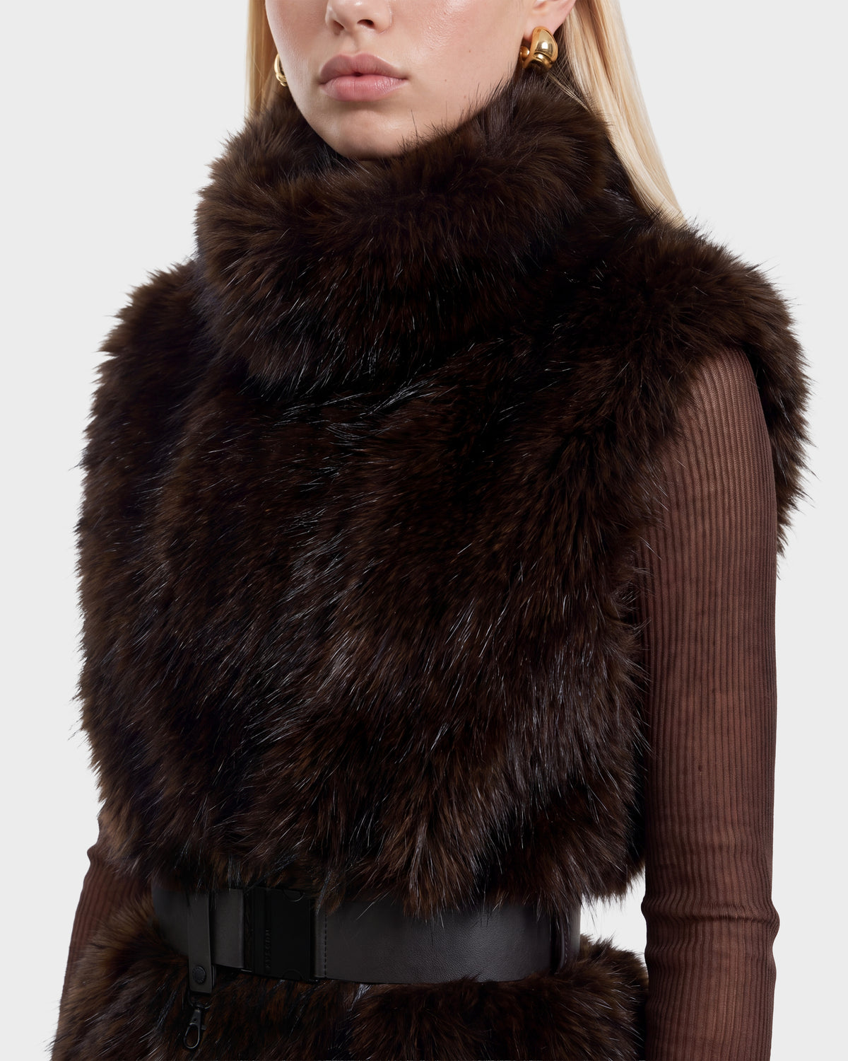 A person wearing a Rudsak MAULIN - 8524611 Mix Espresso faux fur vest with a black vegan leather belt over a ribbed brown mock-neck pullover.