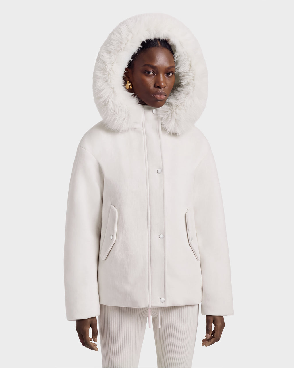 A person wearing a cream-colored Rudsak HAZEL - 8126981 Vanilla wool-blend winter coat with a large, faux-fur trim hood pulled up over their head.