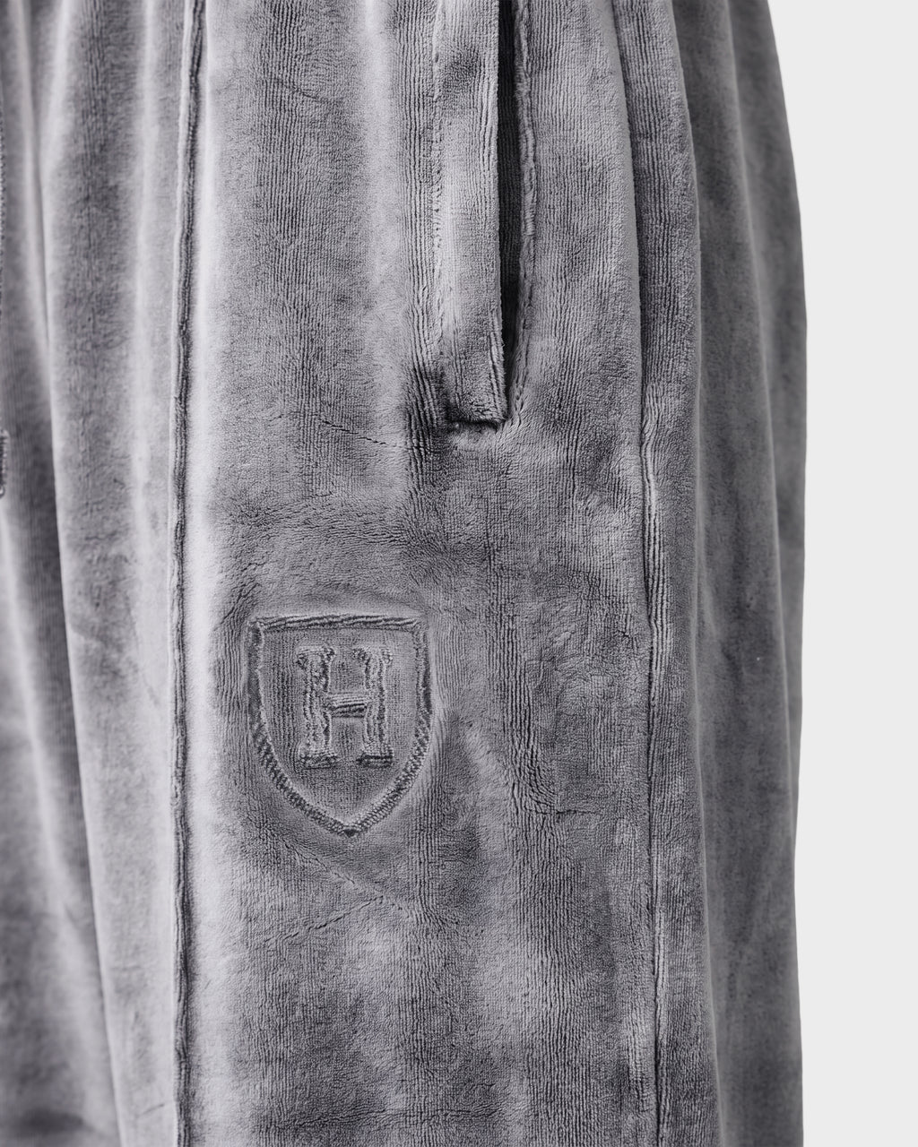 Close-up of the Rudsak OLIVYA HV - H526903 Titanium gray velour pants featuring a side pocket and an embossed shield emblem with the letter H on the upper thigh.