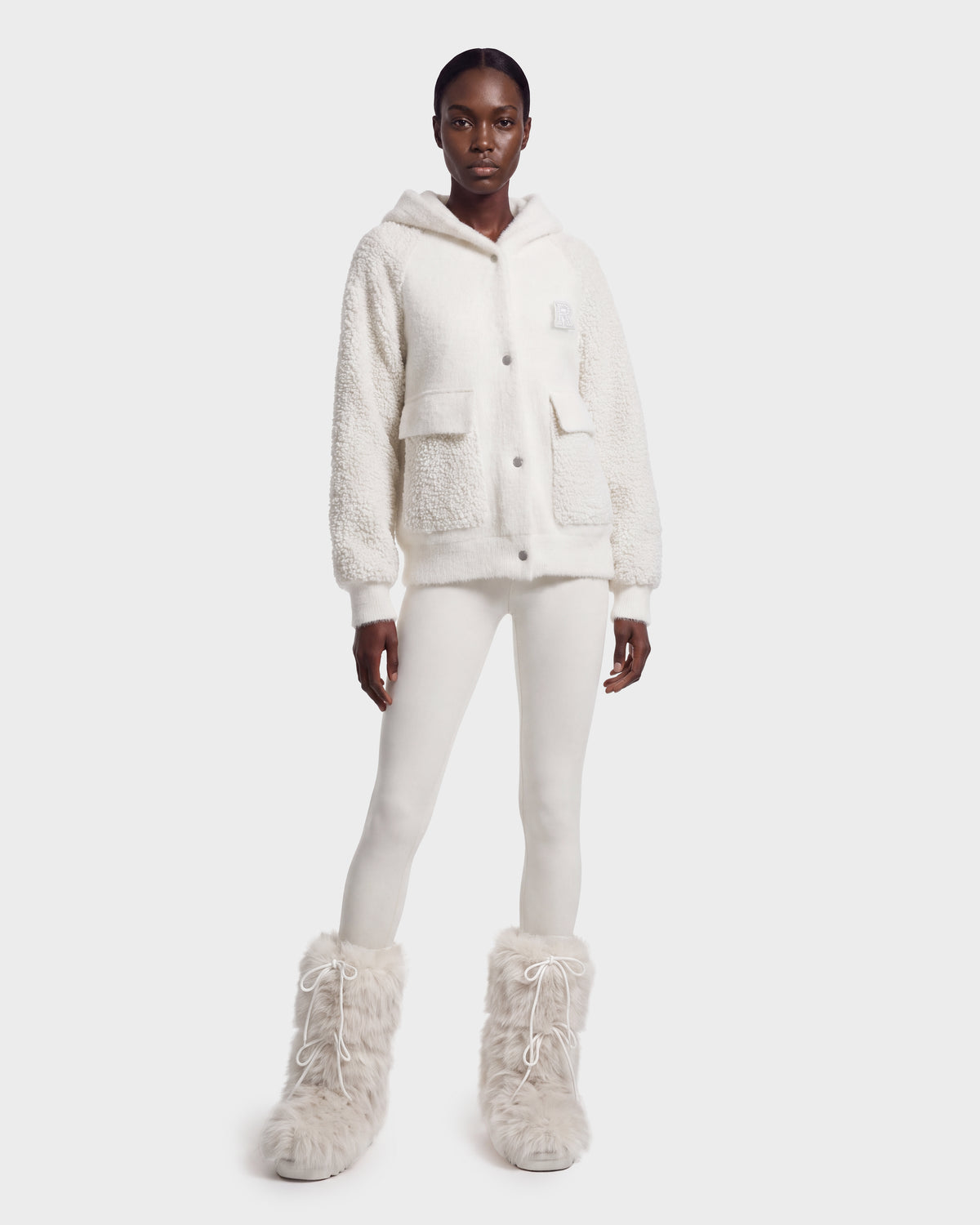 A person stands against a plain light background wearing the Rudsak DAKOTA - 8526515 Iceland cozy white sherpa hoodie, paired with white leggings and fluffy white boots.