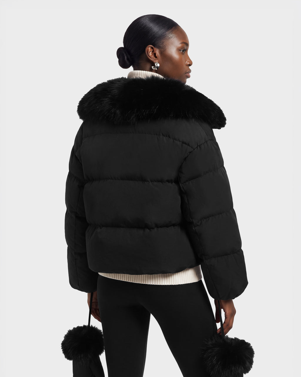 A person seen from behind wearing an ALONDRA - 8126992 Black cropped puffer jacket with a large fur collar and matching fur-trimmed mittens.