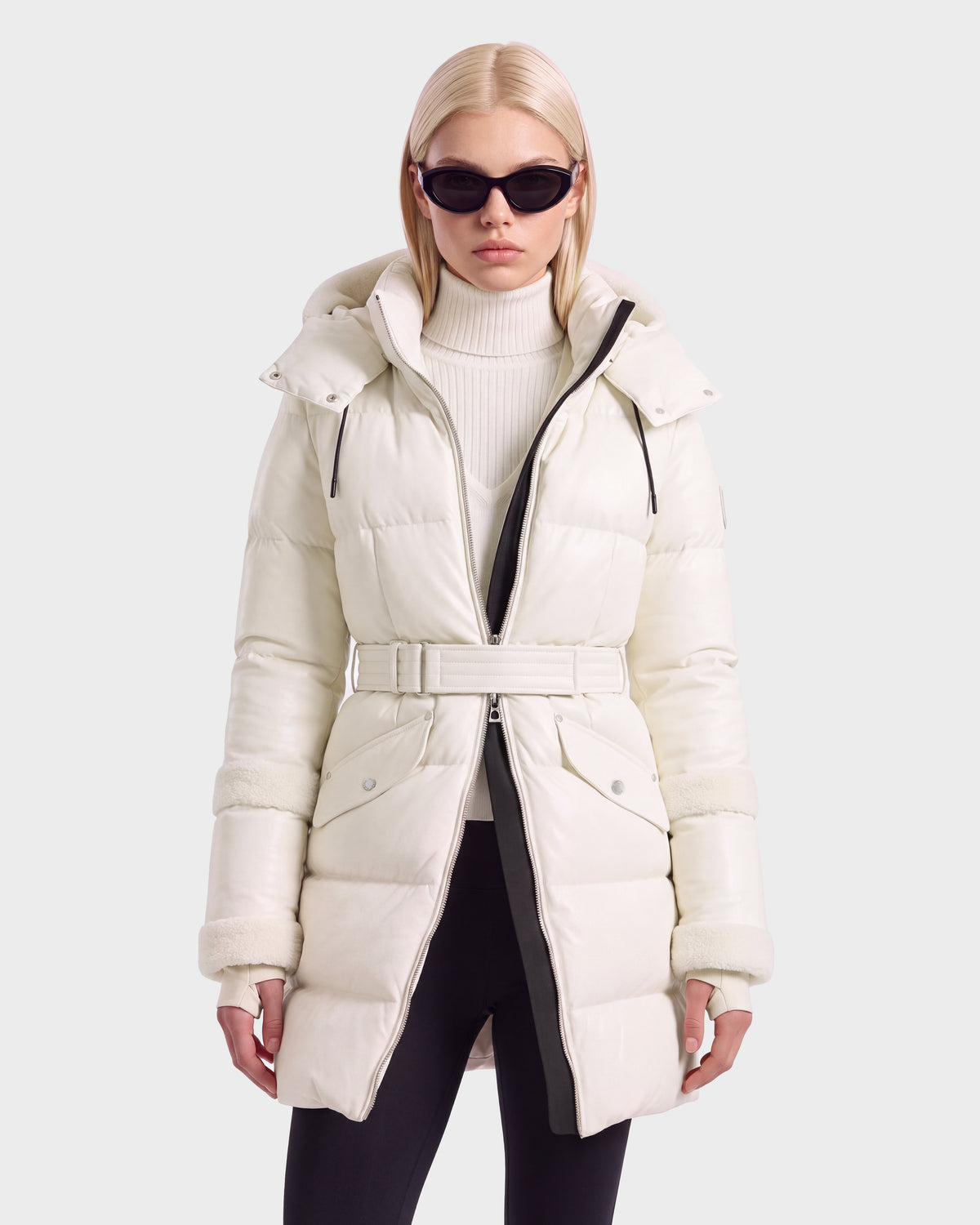 A person wearing a vanilla-colored Rudsak AUDREY L - 8124585 belted down puffer jacket with a hood and black sunglasses.