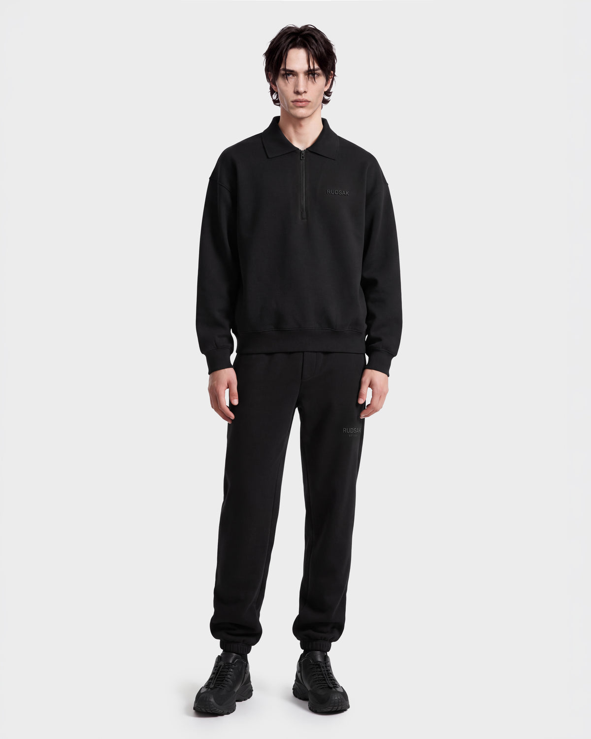 A person faces forward, wearing the Rudsak IDRIS - 6526500 Black pullover with matching black sweatpants and shoes, set against a plain white background.