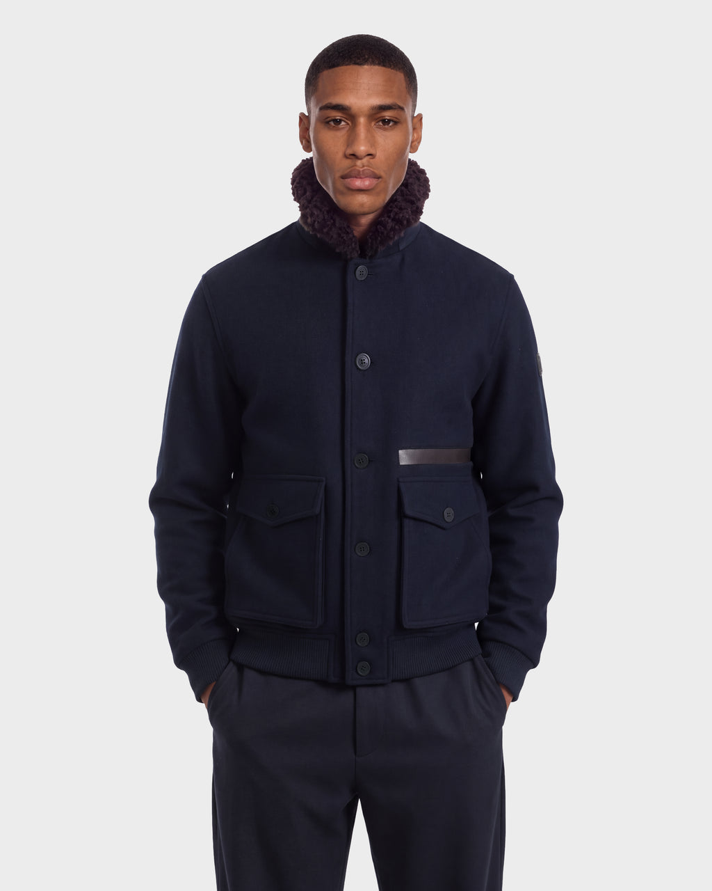 A man wearing a Rudsak JULIUS - 6126723 Navy wool-blend jacket featuring a dark shearling collar and buttoned flap pockets.