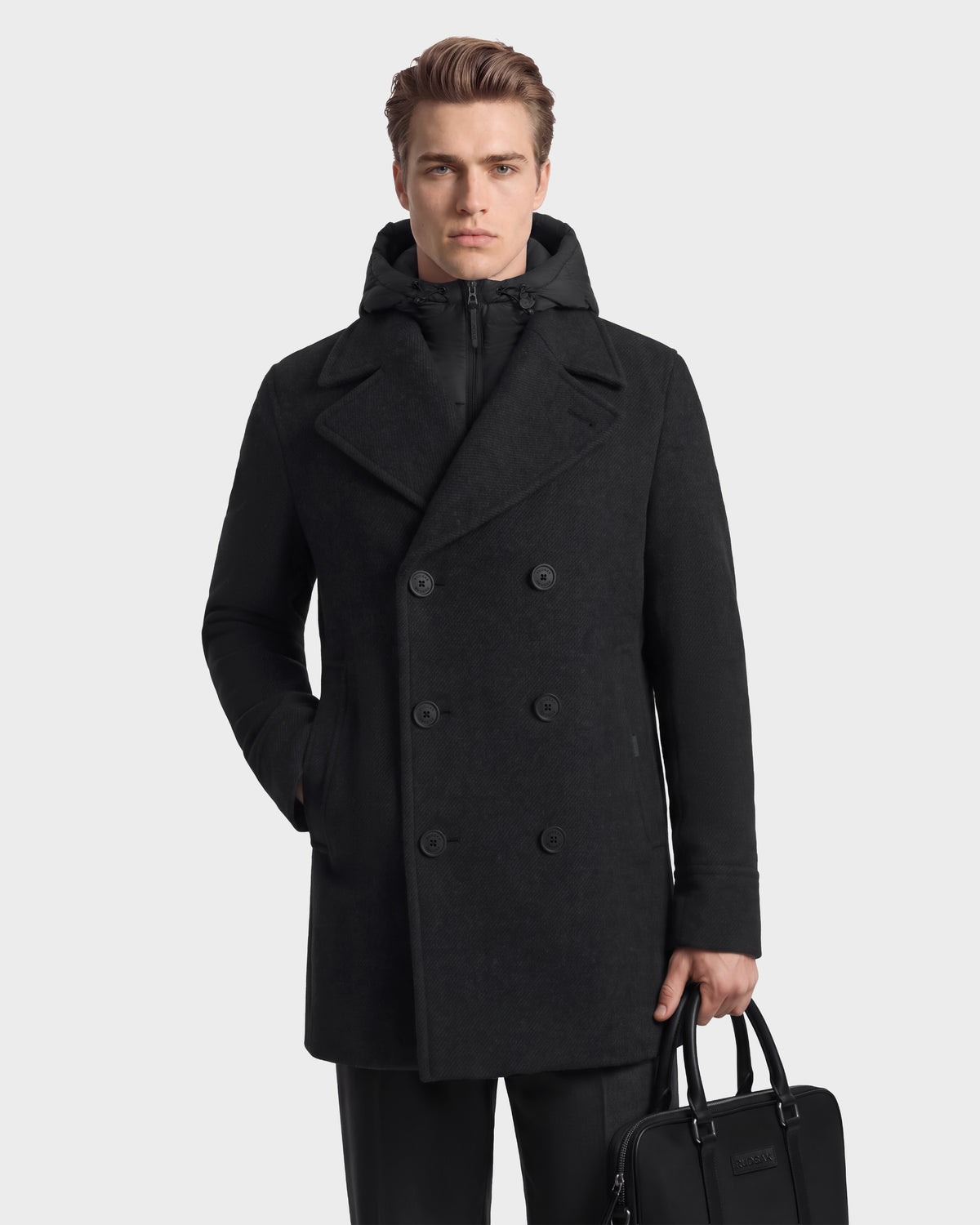 A man wearing a charcoal Rudsak LUCIEN - 6126508 double-breasted pea coat with a detachable hood, holding a black briefcase.