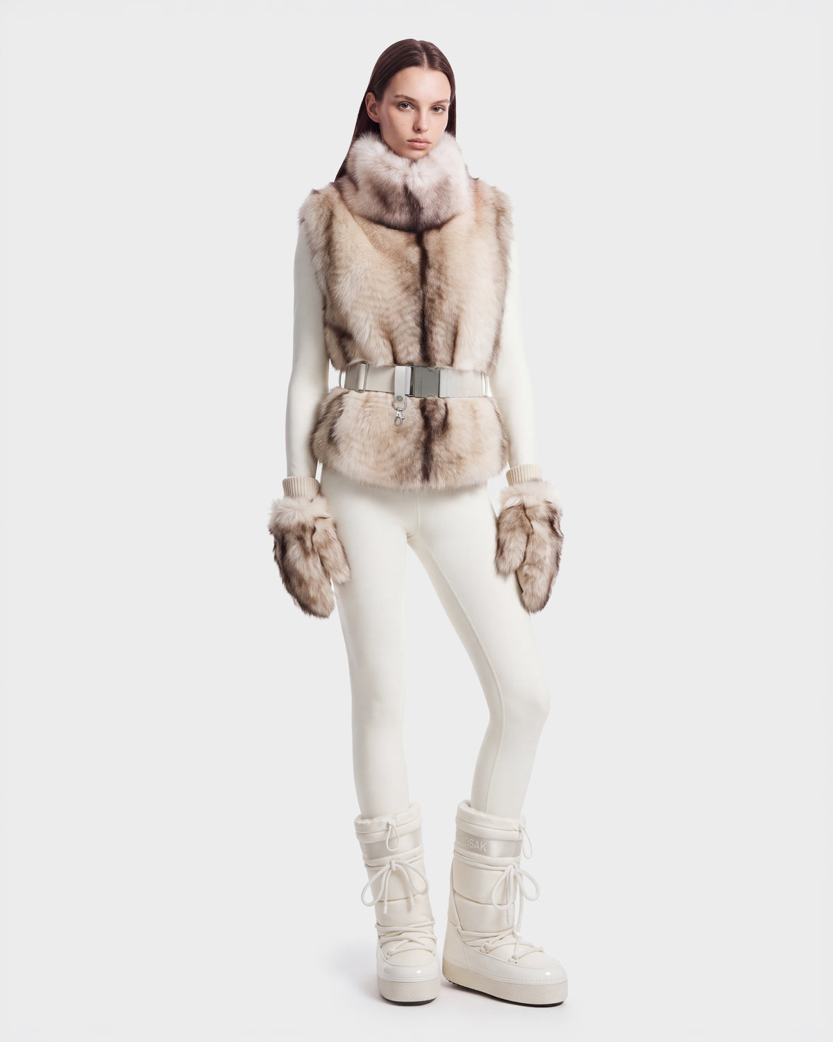 Model wearing a MAULIN - 8524611 Mix Vanilla high-neck faux fur vest over a white mock-neck pullover, matching white leggings, fur mittens, and white winter boots.