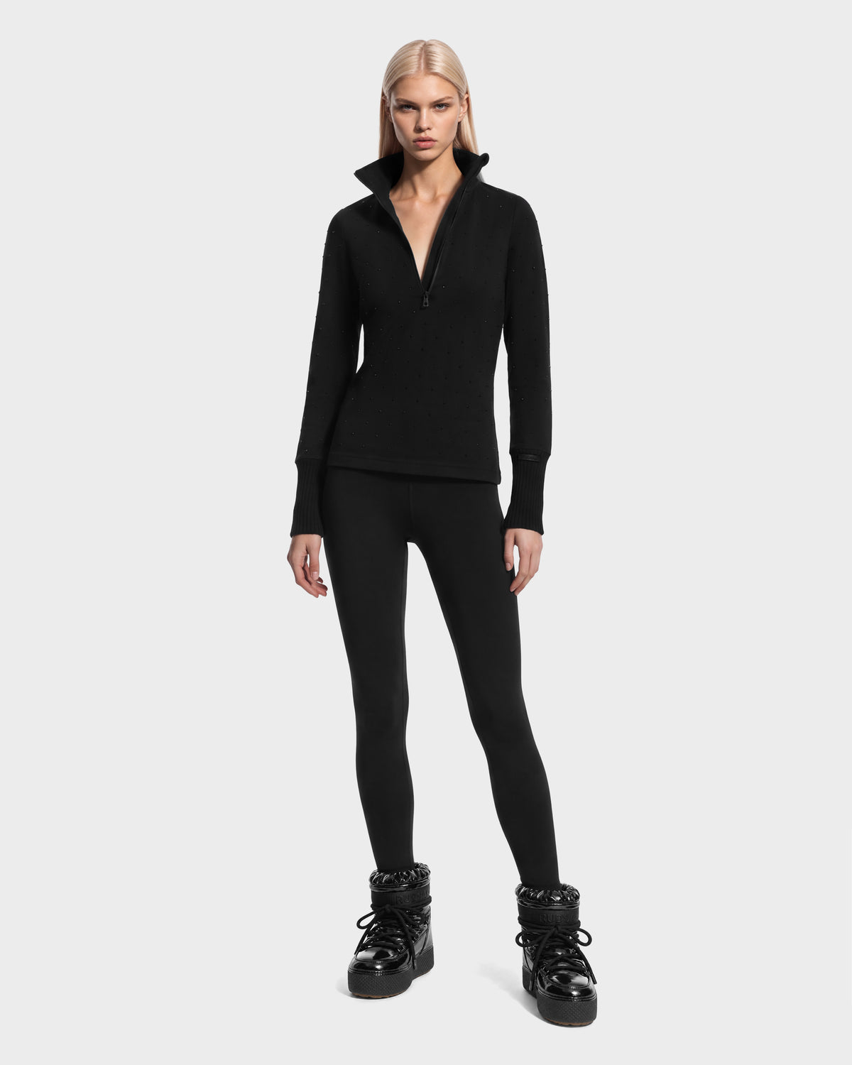 A person wearing a black Rudsak NEVA - 8526524 Black après-ski quarter-zip top, black leggings, and black platform winter boots.
