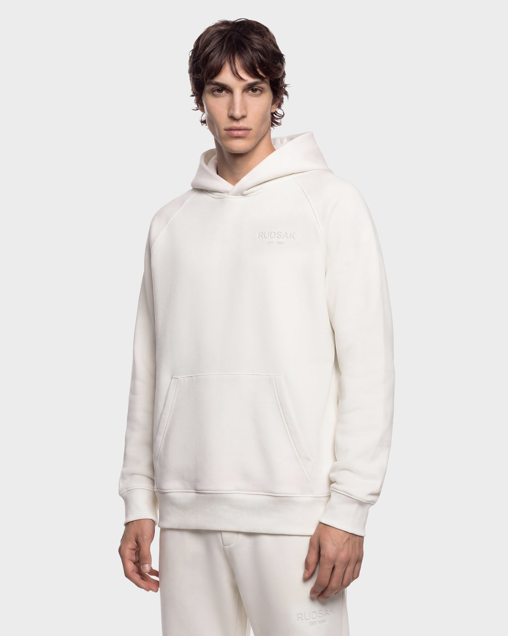 A man wearing a cream-colored RUDSAK BRIAR - 9525001 Vanilla M unisex hoodie with a small logo on the chest.