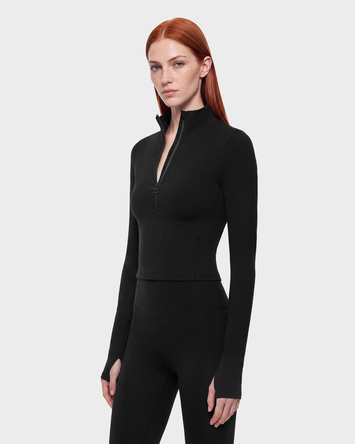A person wearing the Rudsak ANITA - 8526579 Black, a performance-inspired long-sleeve athletic top with a cropped silhouette, a quarter-zip mock neck, and thumbhole cuffs.