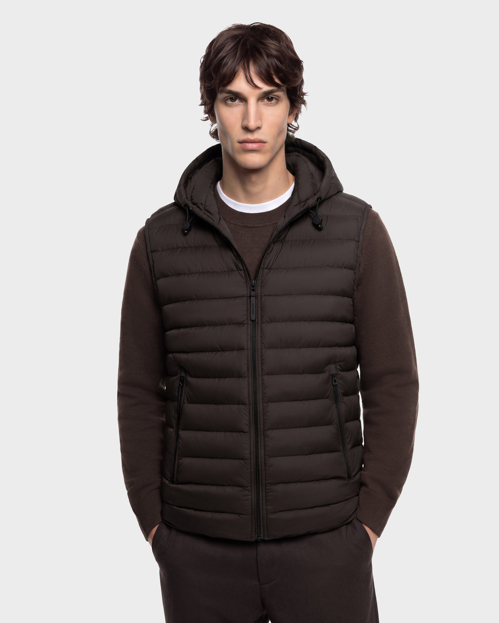 A person wearing a dark brown BRUNO - 6126716 Espresso puffer vest with a hood over a matching brown sweater.