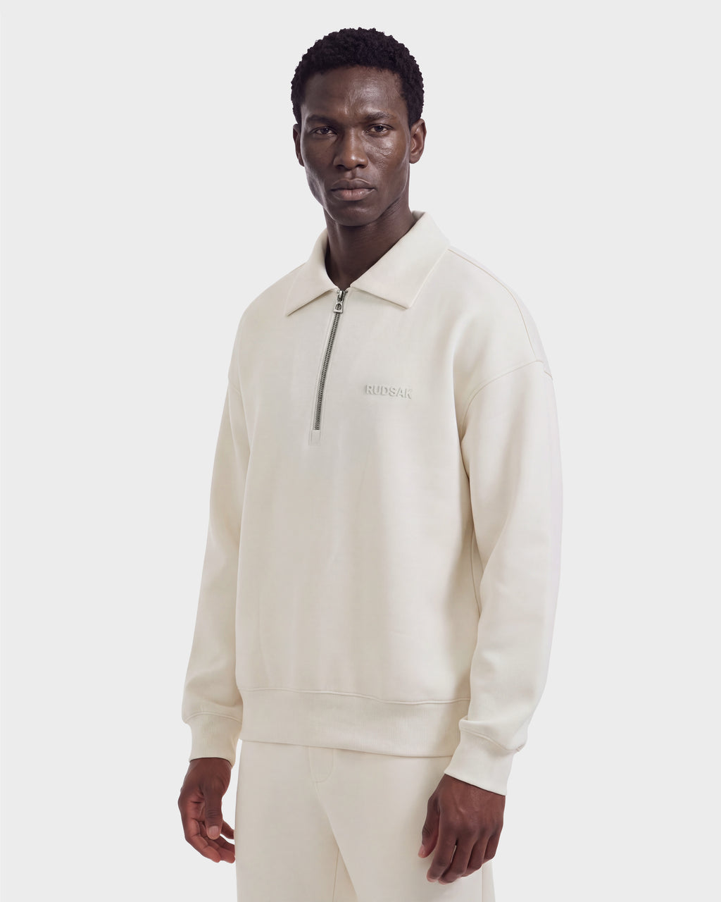A man wears a cream-colored, long-sleeve IDRIS - 6526500 Vanilla quarter-zip polo sweater with a relaxed silhouette and collared neckline.