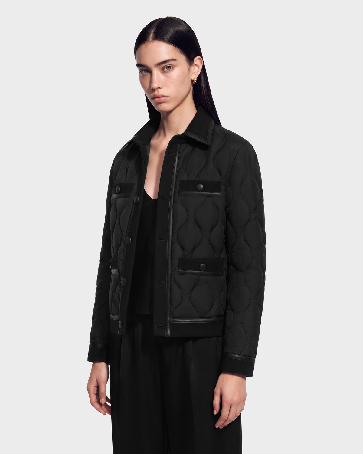 A person wearing a black JOLIE - 8125036 Black RUDSAK quilted down jacket with snap-button pockets over a black top and trousers.