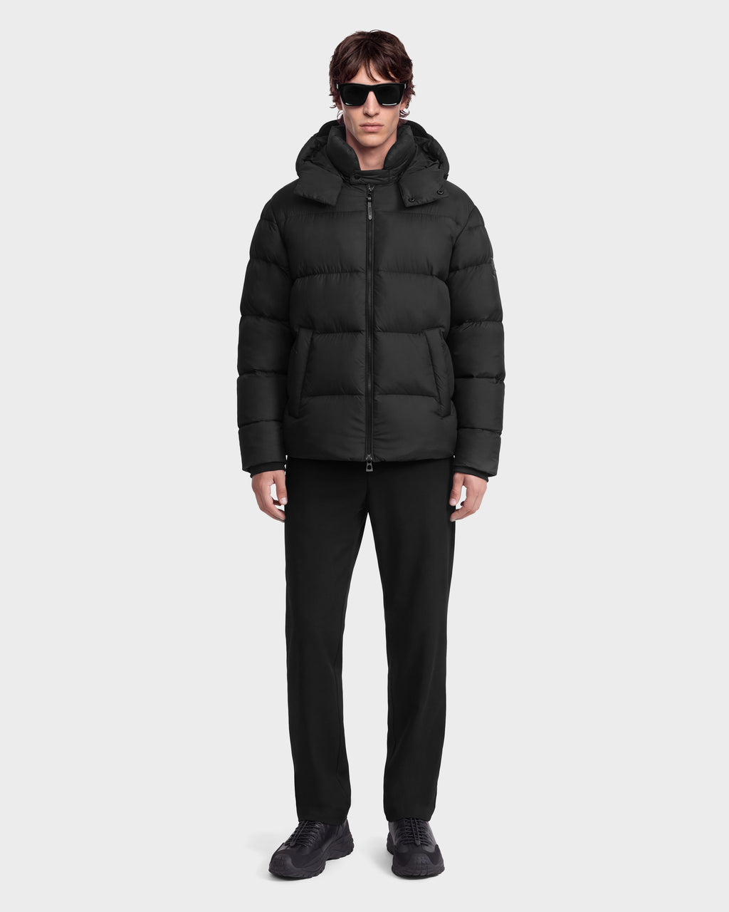 A person wearing a black JASON - 6126803 Black hooded puffer jacket, black pants, black sneakers, and sunglasses.