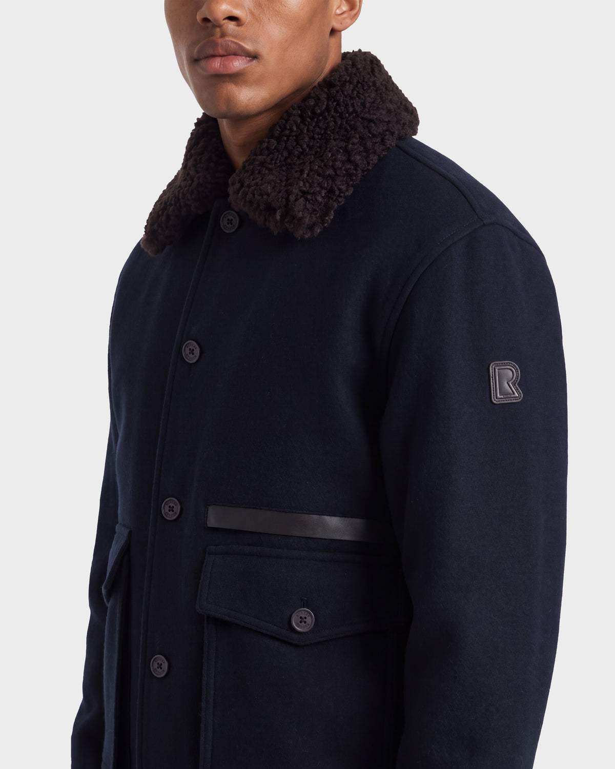 A navy blue Rudsak JULIUS - 6126723 Navy wool coat with a dark shearling collar, button-up front, and two flap pockets.