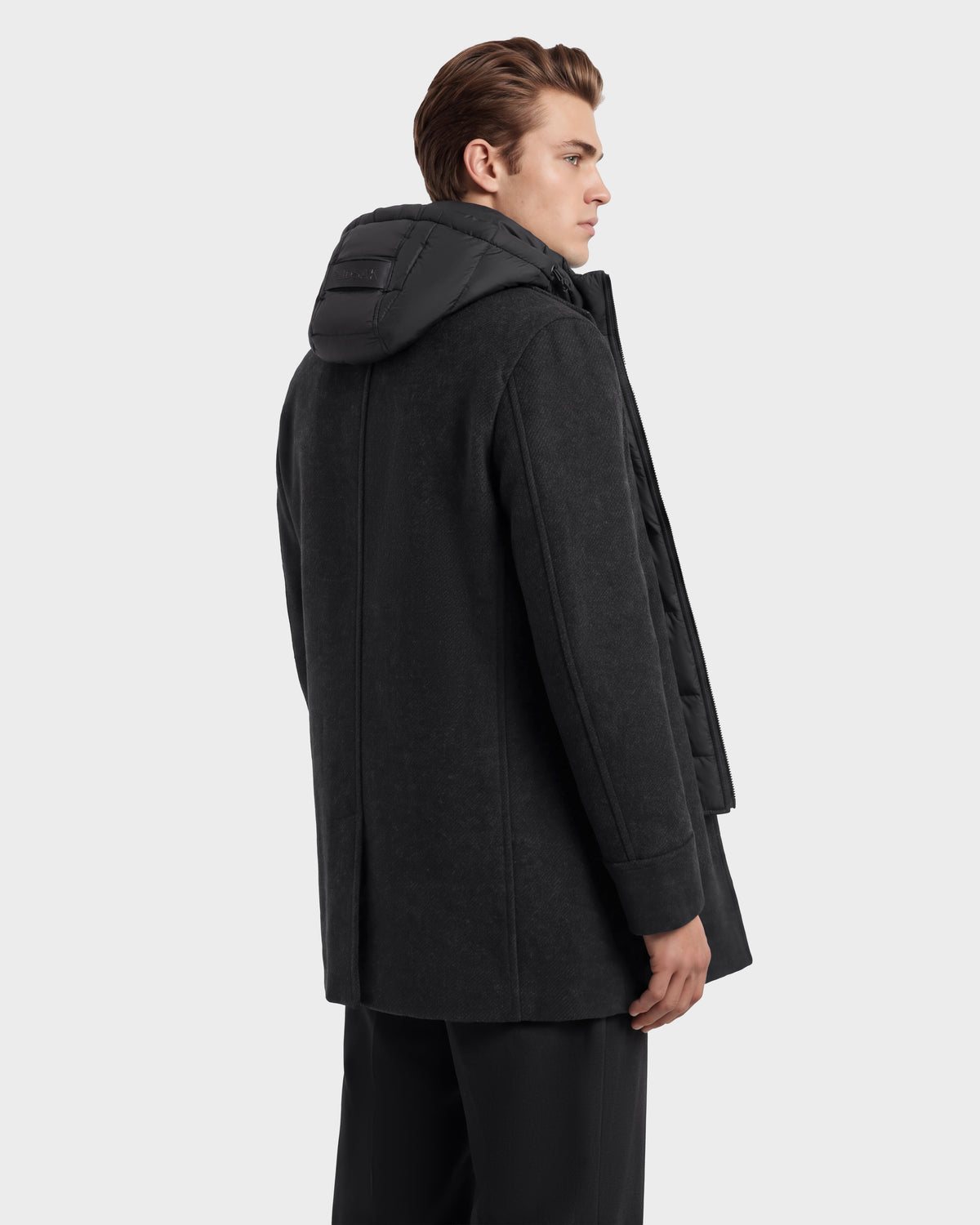 A man wears a Rudsak LUCIEN - 6126508 Charcoal jacket, featuring a black puffer-style hood and a quilted inner layer with duck down insulation.