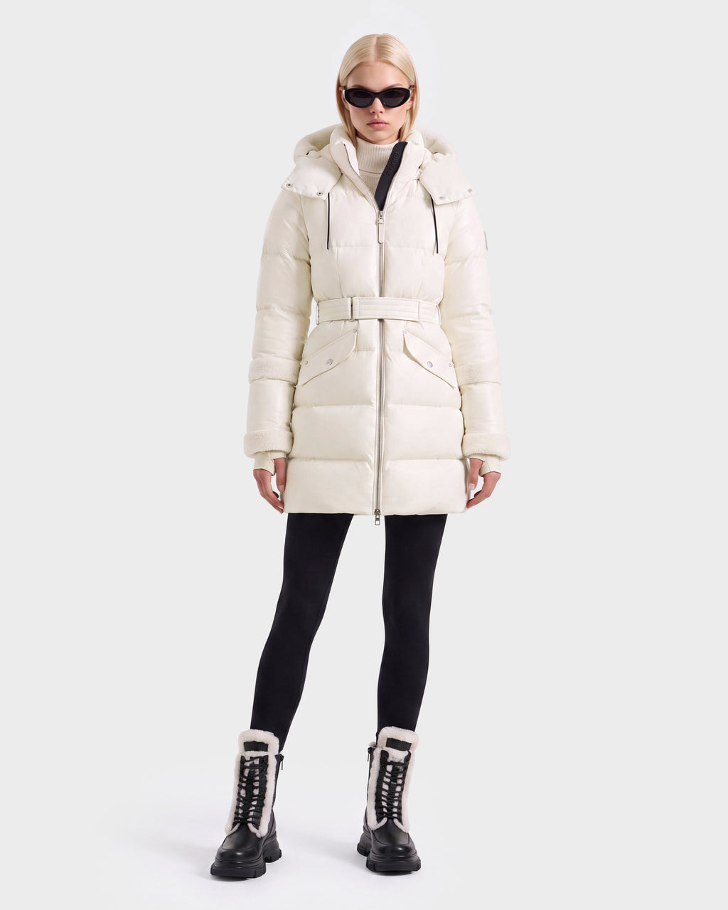 A person wearing a vanilla Rudsak AUDREY L - 8124585 hooded, RDS certified down puffer coat with a belted waist, black leggings, and black lace-up boots with fur lining.