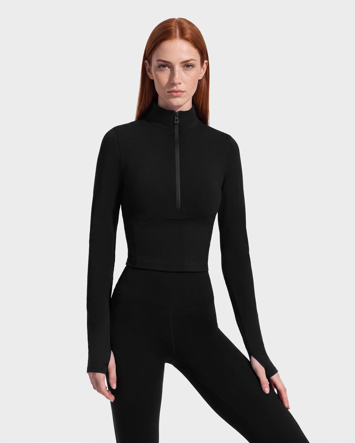 Woman wearing the Rudsak ANITA - 8526579 Black performance-inspired long-sleeve crop top featuring a mock neck, front zipper, and thumbhole cuffs.
