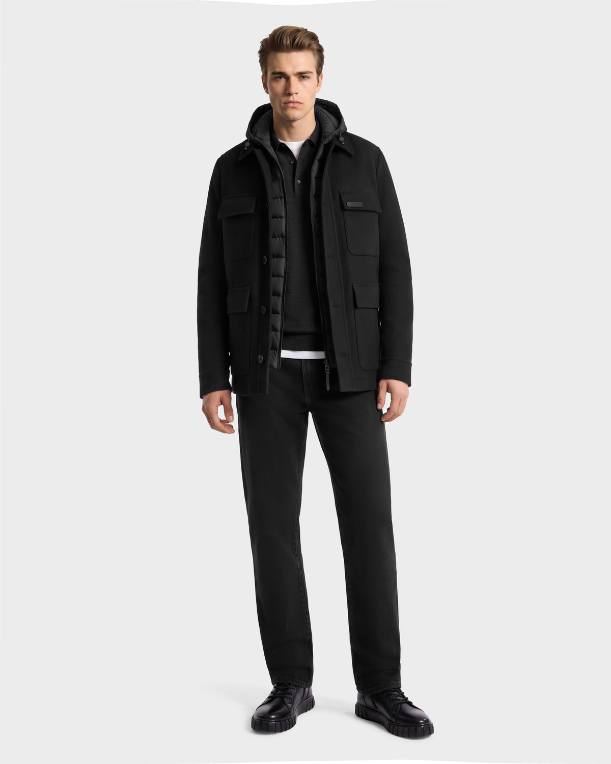 A man wearing a BRUNO - 6126716 Charcoal hooded utility jacket over a black polo shirt, black pants, and black shoes.