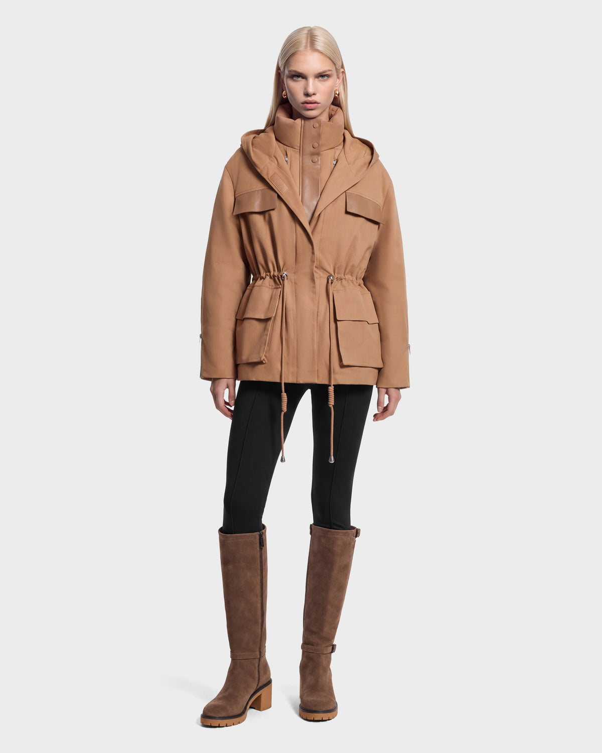 A model wears the ROSALINDA - 8126523 Camel hooded jacket with a cinched waist over black leggings and brown knee-high boots.