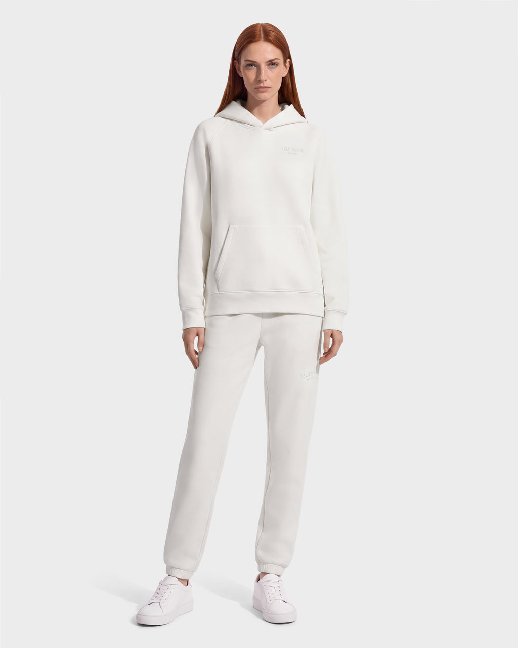 A model wearing a vanilla-colored RUDSAK BRIAR - 9525001 Vanilla W unisex hoodie and matching sweatpants with white sneakers.