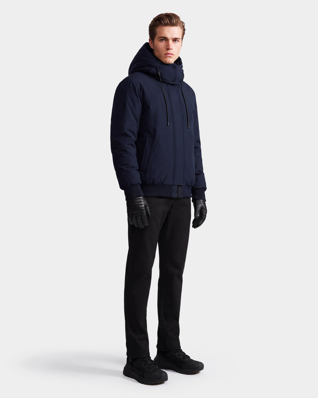 A person stands facing forward wearing the Rudsak WILL - 6126561 Navy winter coat with a hood, paired with black pants, black gloves, and black shoes against a plain white background.