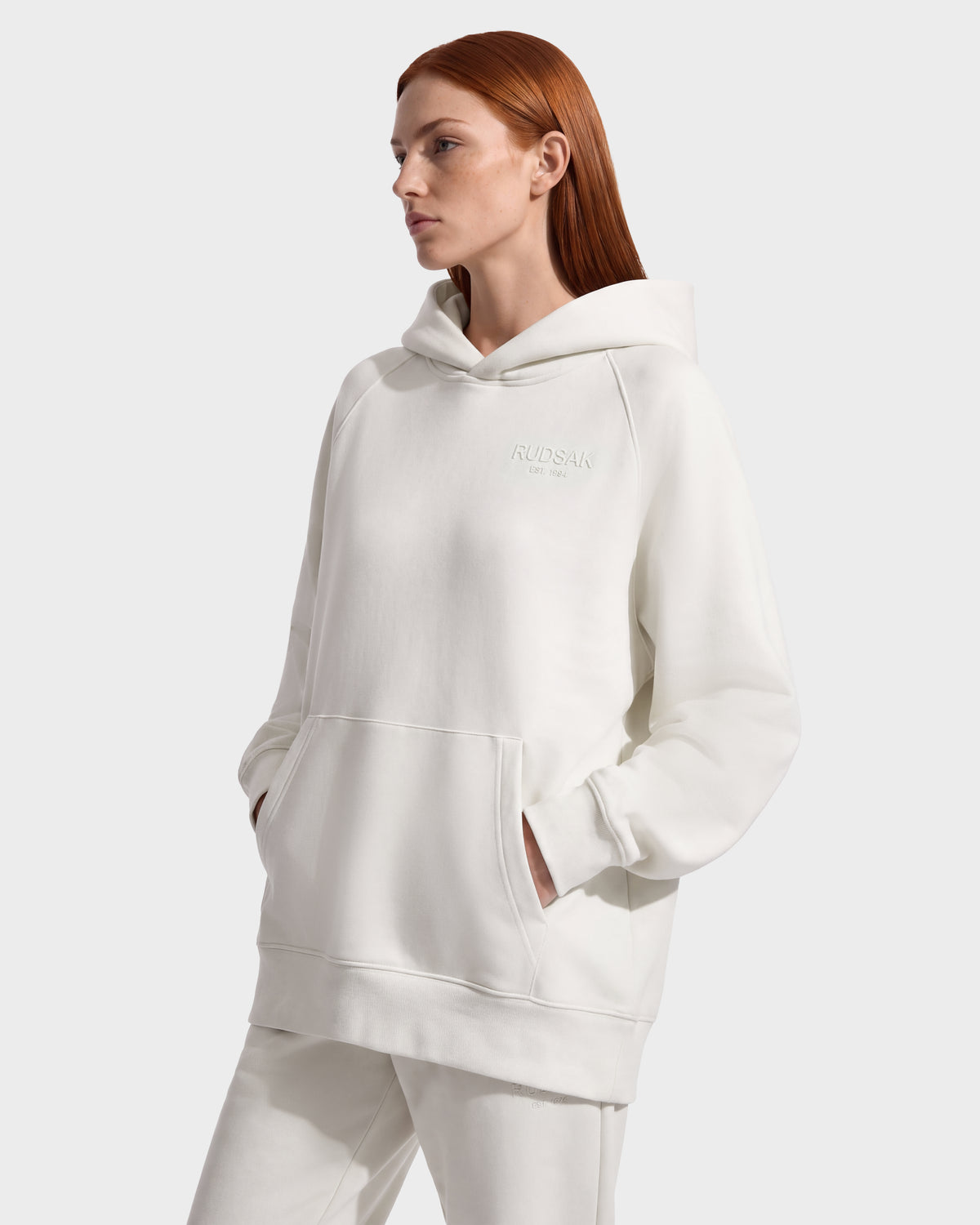 A person wearing an oversized, cream-colored BRIAR - 9525001 Vanilla W unisex Rudsak hoodie with a front kangaroo pocket and a small logo on the chest.