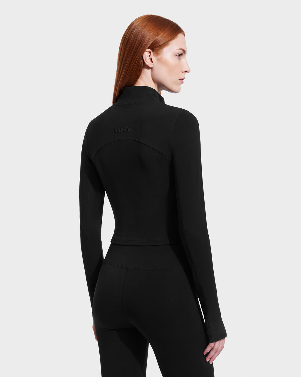 A woman seen from the back wearing the ANITA - 8526579 Black cropped, long-sleeve athletic top and matching black leggings.