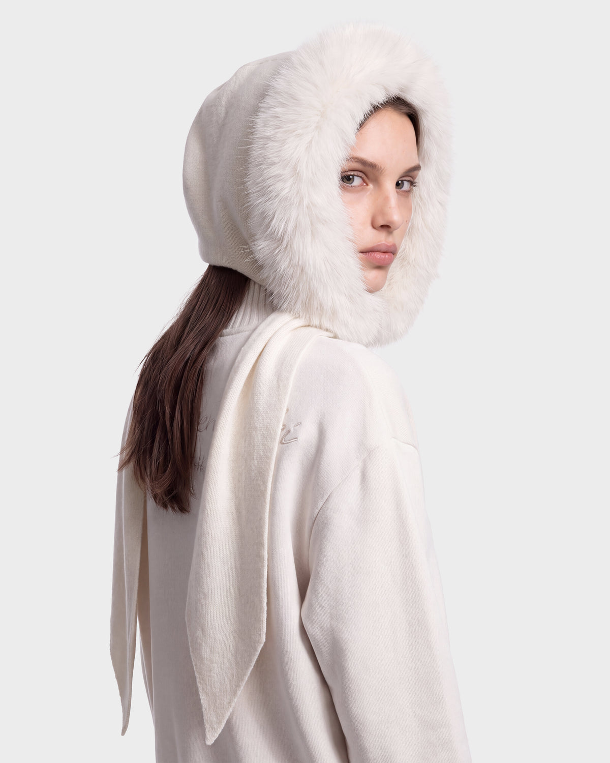 A person wears the Rudsak KARYMA - 8426507 Vanilla, a white outfit featuring a hood lined in white faux fur, and looks over their shoulder toward the camera against a plain light background.