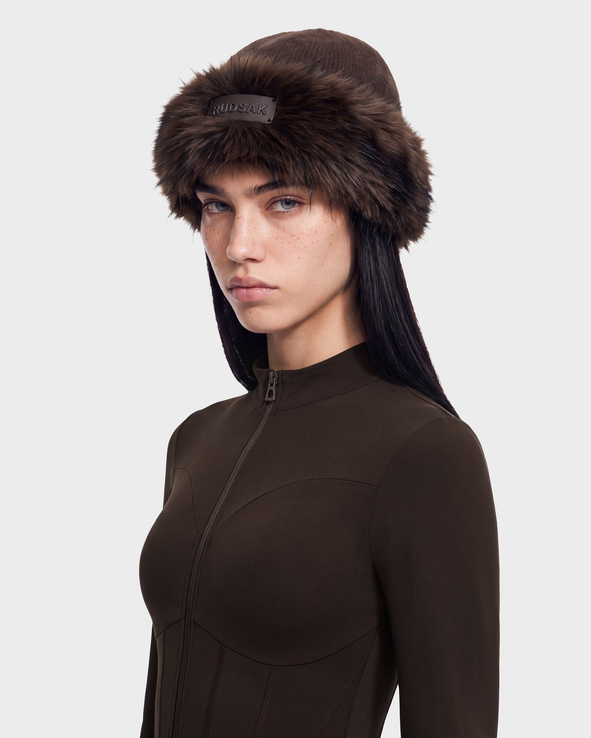 A person wearing a brown faux fur-trimmed beanie and a dark brown zip-up long-sleeved LORETTA W - 8426510 Espresso top from Rudsak.