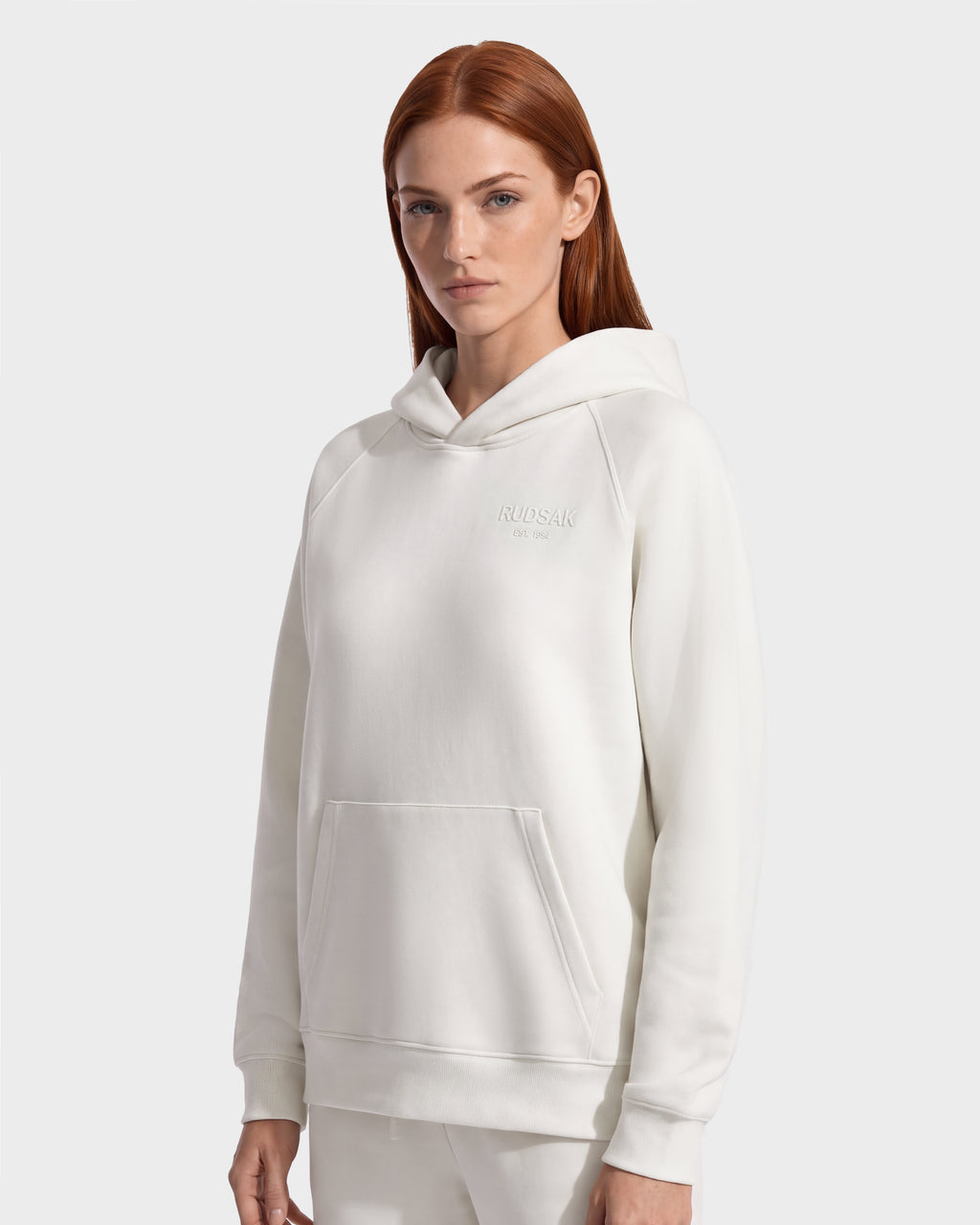 A woman wearing a premium cotton blend, off-white BRIAR - 9525001 Vanilla W hooded sweatshirt by Rudsak with a front pocket and small embroidered text on the chest.
