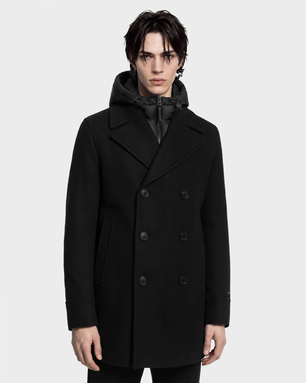 Man wearing a black LUCIEN - 6126508 double-breasted pea coat layered over a duck down insulated hooded vest.