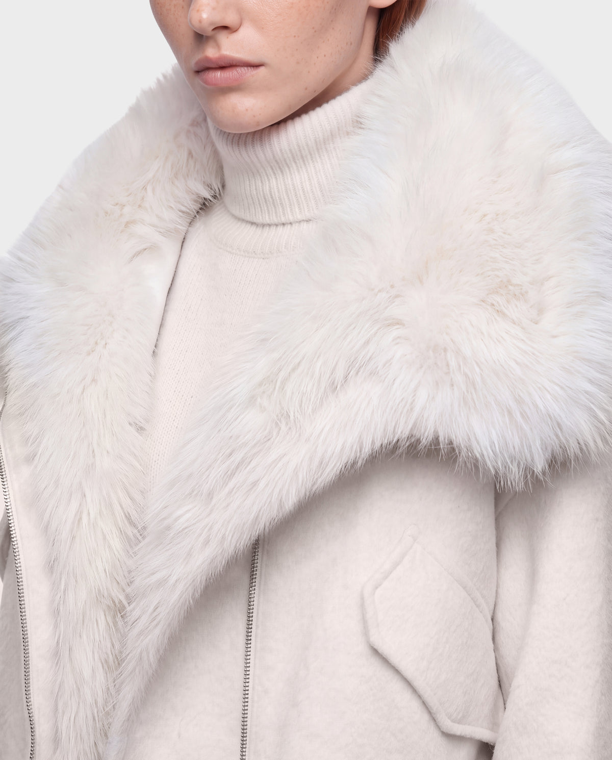 Close-up of a person wearing the Rudsak ZARIA - 8126999 Vanilla puffer coat featuring a large faux-fur collar over a matching cream-colored turtleneck sweater.