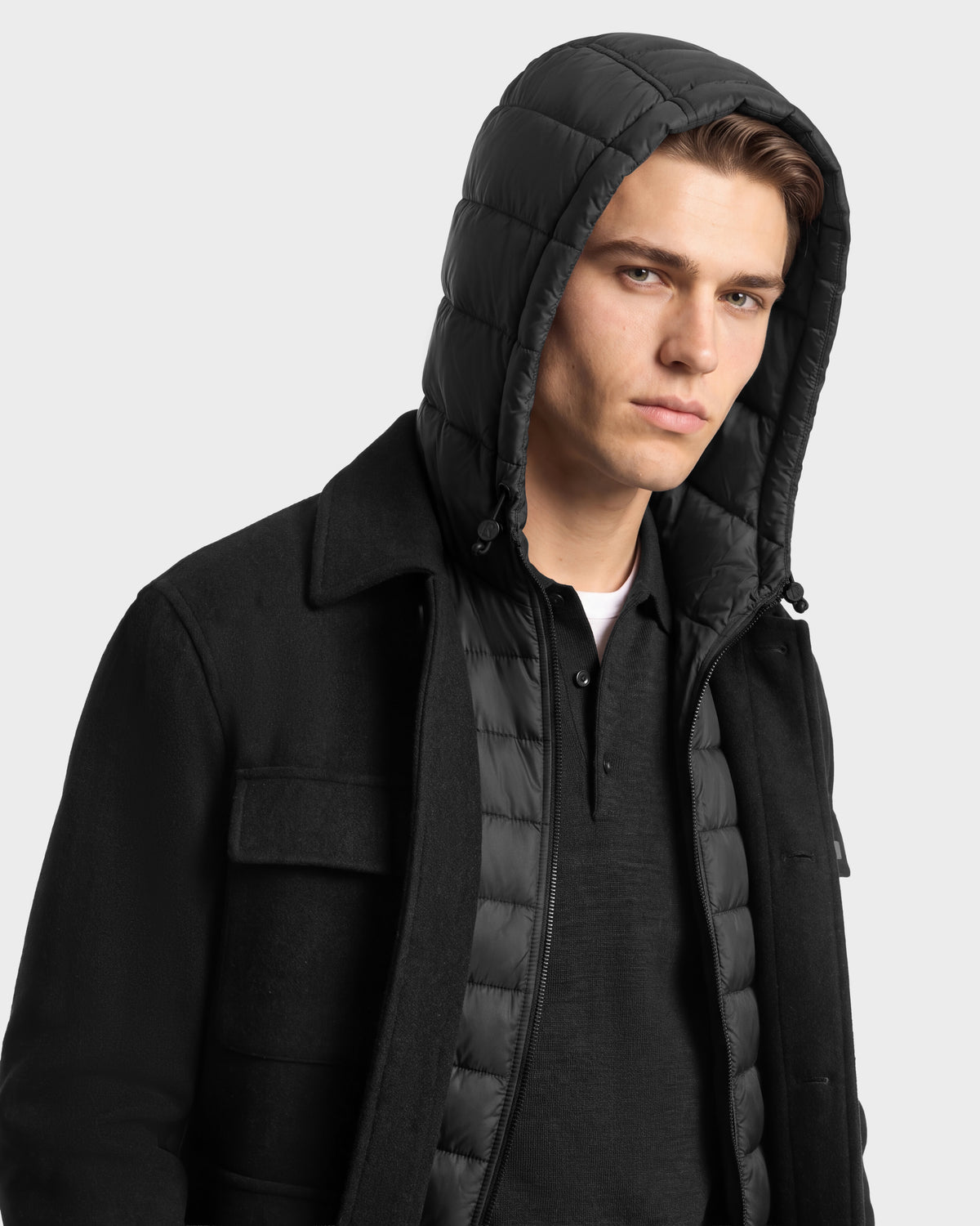 A man wears a charcoal Rudsak BRUNO - 6126716 coat layered over a quilted hooded vest.