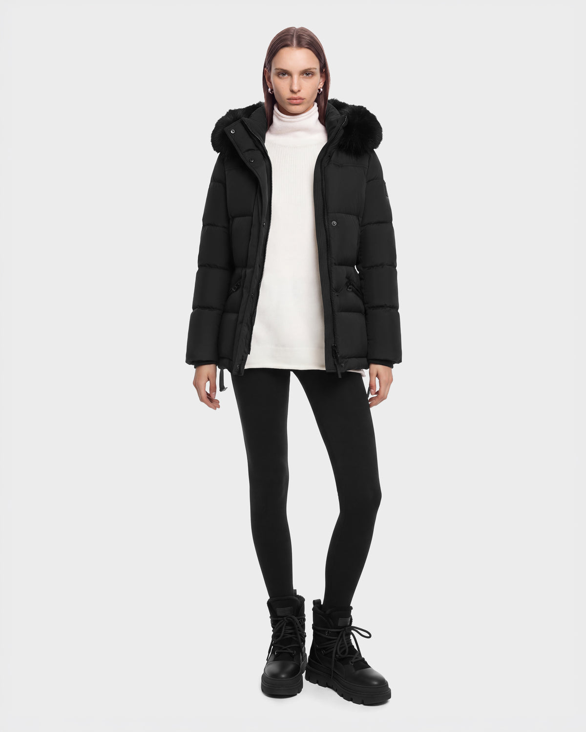 A person wears a black Rudsak GRACE FF - 8126535 Black hooded puffer jacket with fur trim over a white turtleneck, black leggings, and black lug-sole boots.