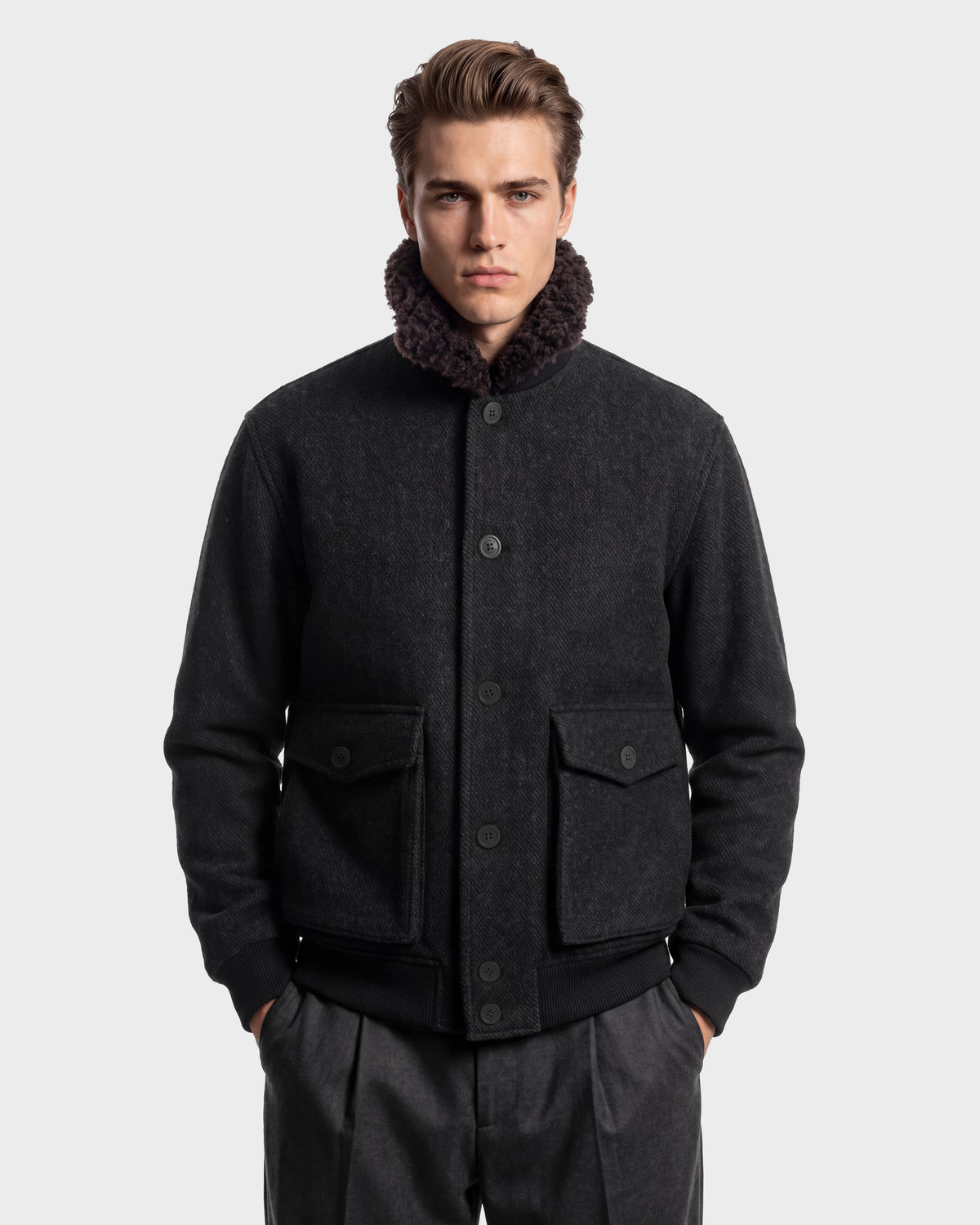 A man wearing a RUDSAK JULIUS - 6126723 Charcoal wool-blend bomber jacket with a dark faux-fur collar and two buttoned flap pockets.