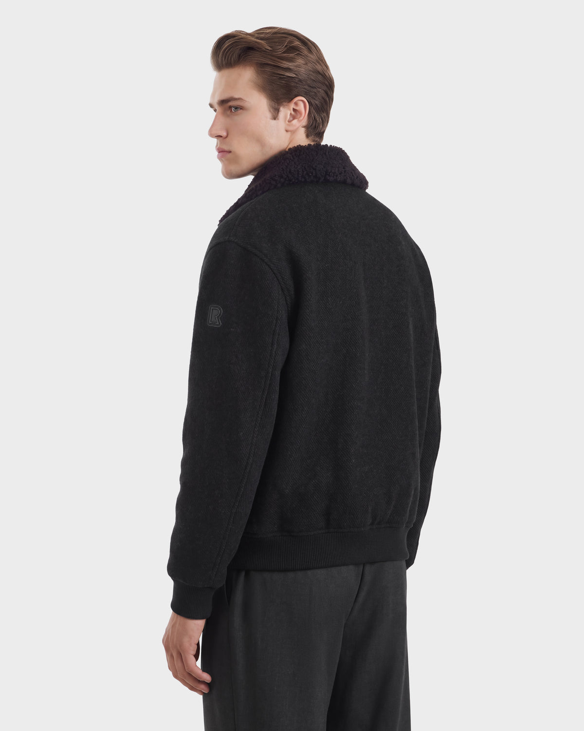 A man wearing a charcoal JULIUS - 6126723 Charcoal bomber jacket with a dark faux-fur collar and ribbed cuffs.