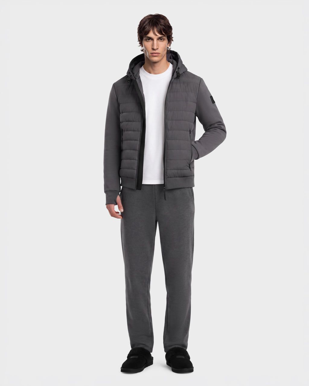 A man wearing a grey DEE MAT - 6124028 Grey hooded puffer jacket over a white t-shirt, matching grey sweatpants, and black slip-on shoes.