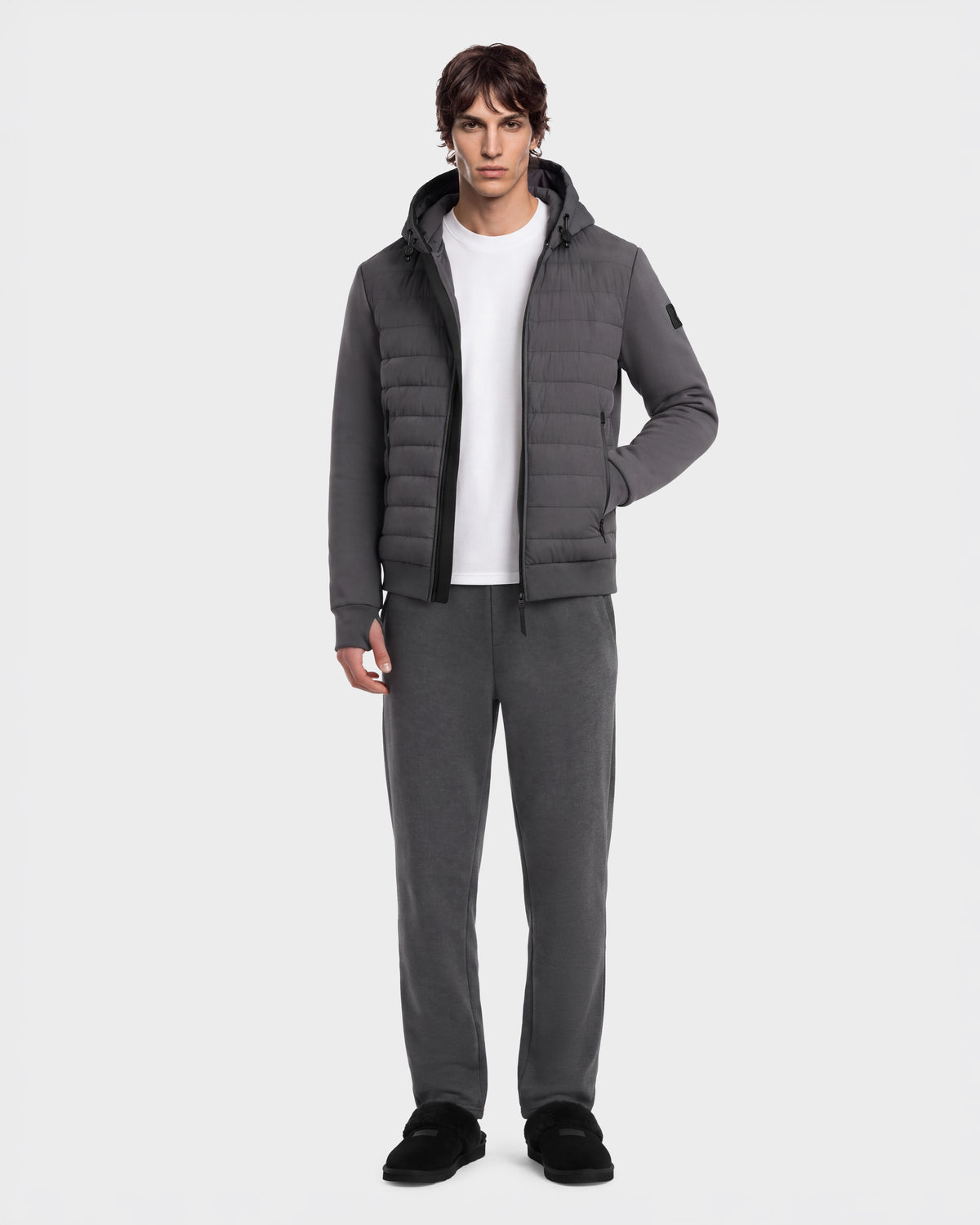 A man wearing a grey DEE MAT - 6124028 Grey hooded puffer jacket over a white t-shirt, matching grey sweatpants, and black slip-on shoes.
